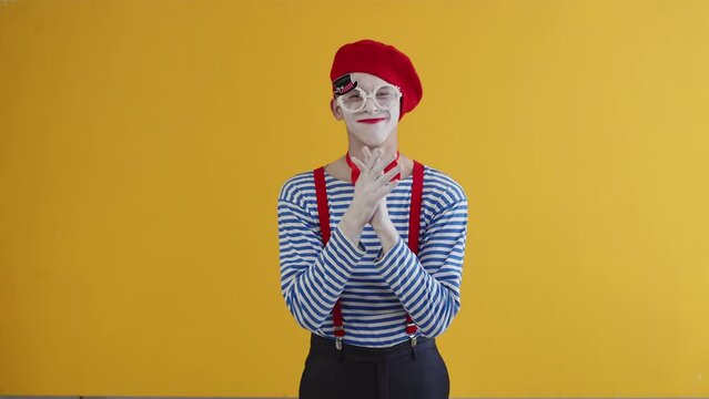 A greedy mime man wearing white makeup, striped shirt and red hat and suspenders rubbing his hands together with a satisfied, wily, cunning expression on his face. Concept of fraud, deception