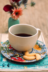 Xicara com pirex encima de livro, flores, biscoitos e café da manha na mesa com cadeira