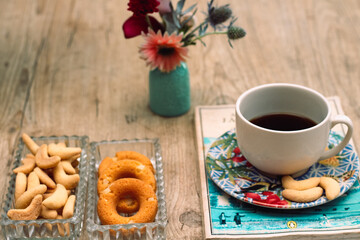 Xicara com pirex encima de livro, flores, biscoitos e café da manha na mesa com cadeira