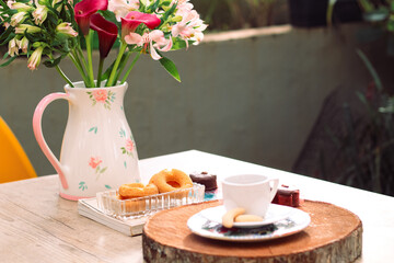 Xicara com pirex encima de livro, flores, biscoitos e café da manha na mesa com cadeira