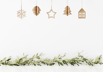 Simple minimal Christmas wall mockup with wooden hanging decoration and green garland of branches on empty white background. 3d illustration, 3d rendering