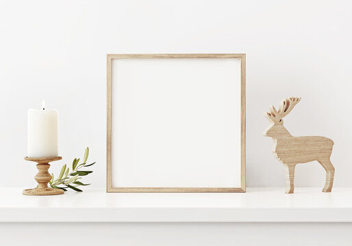 Brown square frame mockup in white interior with simple minimal Christmas decoration, candle and wooden deer. 3D rendering, illustration.
