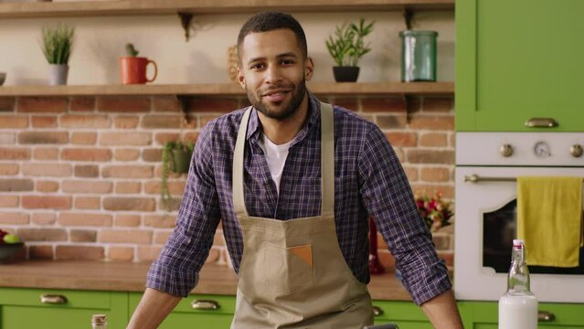Charismatic and handsome guy looking posing in front of the camera at the kitchen he smiling very cute and wear the kitchen apron