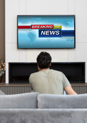 Back view on excited man sitting on the couch and watching breaking news on tv at home