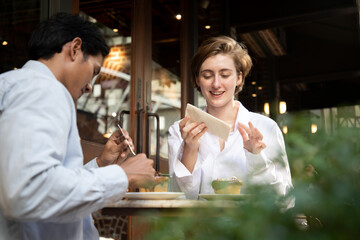 Man and charming woman having business lunch at restaurant sitting at table eating fresh bread,chocolate and hot espresso talking smiling cheerful outside restaurant