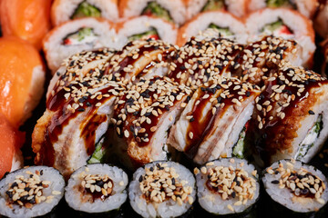 Close up of sushi rolls drizzled with sauce and sprinkled with sesame seeds.