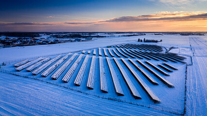 Naklejka na ściany i meble Frozen photovoltaic farm in winter at sunset, aerial view