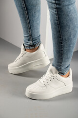 Cropped image of stylish sneakers on women's feet on white and gray background.