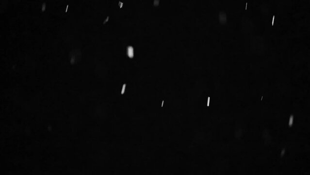 Bokeh of white snow hd slow motion video on a black background. Falling snowflakes on night sky background, isolated for post production and overlay in graphic editor.