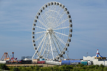 Tall ferris wheel and other amusements on a pier over the beach and near a wooden boardwalk