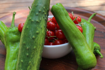 Some tiny cherry tomatoes and green peppers in white plates on wooden concept.