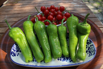 Some tiny cherry tomatoes and green peppers in white plates on wooden concept.