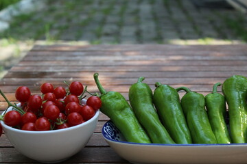 Some tiny cherry tomatoes and green peppers in white plates on wooden concept.