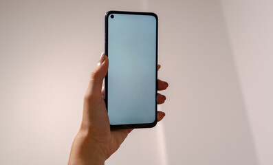 Woman hand holding phone on white background with copy space. Woman holding smartphone with white screen. Close up of hand with blank mobile phone screen