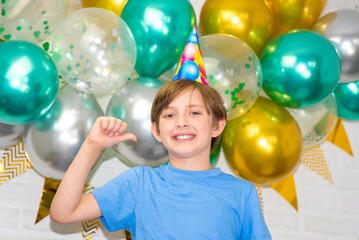 Fototapeta na wymiar happy boy in a birthday hat on the background of balloons at home