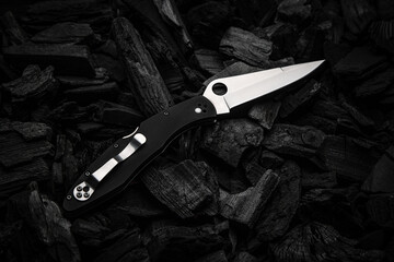 Modern knife with a silver blade. Hunting, military folding knife on smoldering charcoal. Black back.