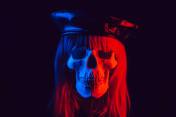 human skull of a woman in a wig with hair in a hat with colored red and blue light on a black...