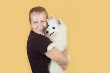 Beautiful joyful mature woman hugs her reliable friend - white spitz dog, woman is happy to have someone to talk to, woman with dog in her arms on yellow background
