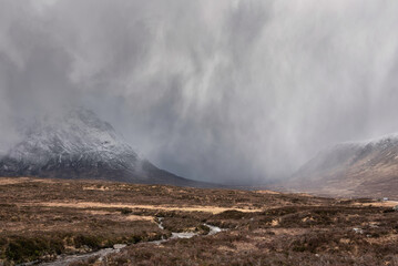 Beautiful Winter landscape image of Stob Dearg Buachaille Etive Mor viewed from Rannoch Moor with snowcapped peak with heavy snow fall passing by the mountain