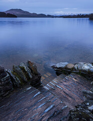 Beautiful landscape image of Loch Lomond and snowcapped mountain range in distance viewed from small village of Luss