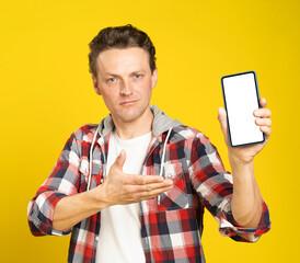 New app or website introduction holding smartphone with white screen blond man, wearing red plaid shirt. Man with phone display mock up isolated on yellow background. Mobile app advertisement