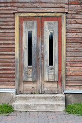 Old red wooden doors, entrance to wooden house with withered peeling paint on the walls. Tartu, Estonia. European historic architectural details.
