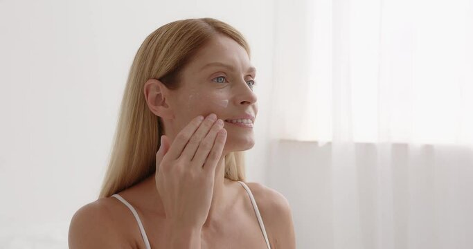 Woman applies anti aging cream on face undergoes beauty treatments cares about skin