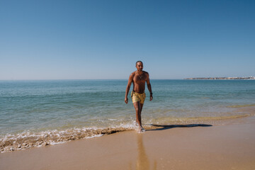 Fototapeta na wymiar BOY COMING OUT OF THE SEA ON HIS VACATION AND WALKING ON THE BEACH