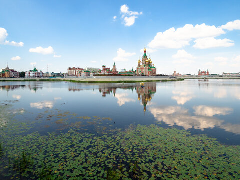 surface Malaya Kokshaga river overgrown with green water lily leaves and view of Voskresenskaya embankment with Cathedral of the Annunciation of the Blessed Virgin Mary in Yoshkar-ola city in summer © Ekaterina