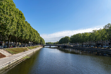 Fototapeta na wymiar Caen, France - 24 July 2022: River Orne and its two banks with numerous plane trees with lush green crowns in sunny weather, Normandy.
