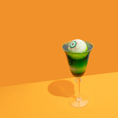 Halloween spooky green cocktail with  bloody eyes on trendy orange background. Festive drink. Halloween party.