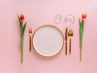 Festive pink table setting. Pink plate with gold cutlery and red tulip on pink background....