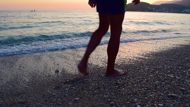 Man slowly walks along beautiful pebble beach of Himare town at sunset. Ionian sea. Albania. Summer cloud landscape. Concept of summer holidays and relaxation.