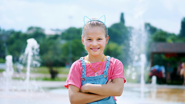 portrait of a smiling, happy eight-year-old girl in a fun hoop with ears on her head, hair ornament. on the background of fountains, summer, hot day during the holidays. High quality photo