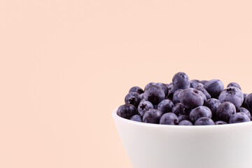 Beautiful fresh blueberries in a white bowl on a beige background with copyspace. Vegan and vegetarian concept. Summer healthy food.