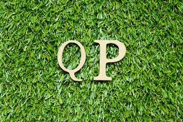 Wood alphabet letter in word QP (Abbreviation of Quality procedure) on green grass background