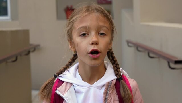 School-age girl is talking, looking at a webcam, reading the text of poems, standing on the porch at home