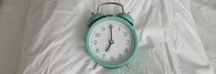 Alarm clock for seven o'clock on white pillow on bed