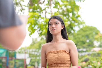 A female Asian teen puts on a blank face as she listens to her angry uncle pointer at her, outside in the garden. - obrazy, fototapety, plakaty