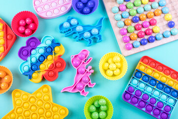 Set of trendy colorful fidget toys pop it and wooden clip beads board game on blue background. New sensory antistress and thinking logic toys for children and adult. Flat lay.
