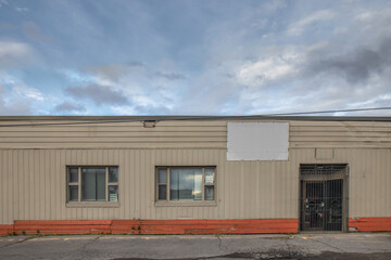 Facade of an abandoned and rundown one storey flat roof commercial building, dented metal siding,...