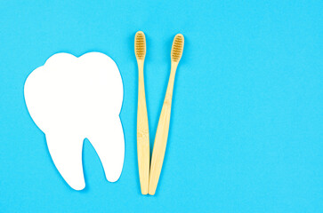 White tooth and wooden toothbrush on a blue background. Dental care concept, copy space