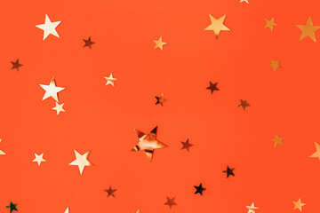 Golden stars glittering confetti on red background. Trendy festive holiday backdrop. Many star-shaped particles for a postcard, invintation or web banner. 2023 merry xmas backplate