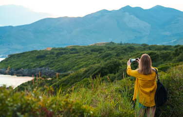 Woman with backpack photographs the mountains at sunset.