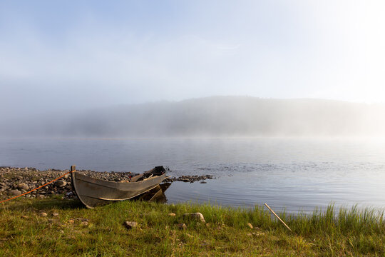 Wooden fishing boat in the morning in Teno river in Lapland, Finland. In the background there is fog and a misty forest.