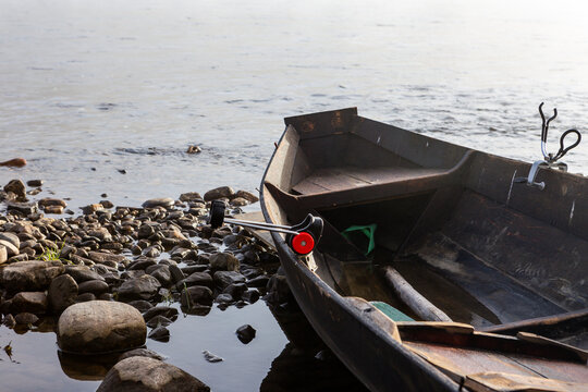 Half of a brown wooden fishing boat in the Teno river in Lapland, Finland. On the left side, round stones.