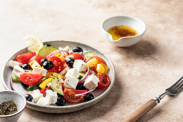 Fresh vegetable greek salad with feta cheese, tomatoes, red onion, cucumber, pepper, olive oil and italian herbs served on brown background with rustic fork