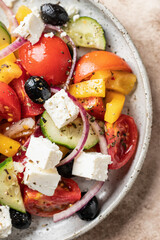 Fresh vegetable greek salad with feta cheese, tomatoes, red onion, cucumber, pepper, olive oil and italian herbs close up. Top view