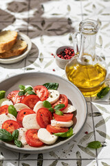 Plate of delicious Caprese Salad with Mozzarella Cheese, Tomatoes and Basil In bright sunlight with hard shadows on printed tile background