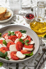 Plate of delicious Caprese Salad with Mozzarella Cheese, Tomatoes and Basil In bright sunlight with harsh shadows close up on printed tile background